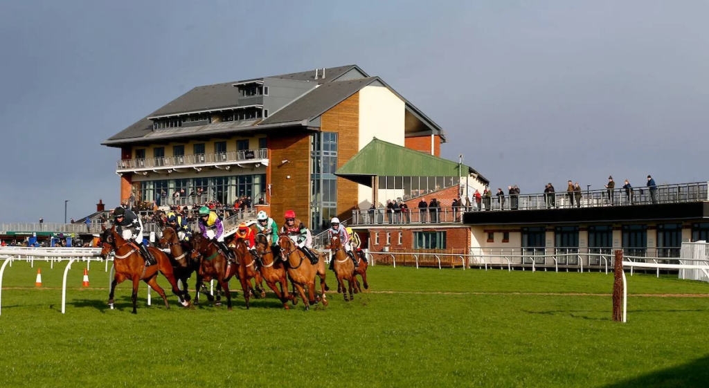 Action-packed horse racing at Carlisle Racecourse with jockeys competing and spectators watching from the grandstand